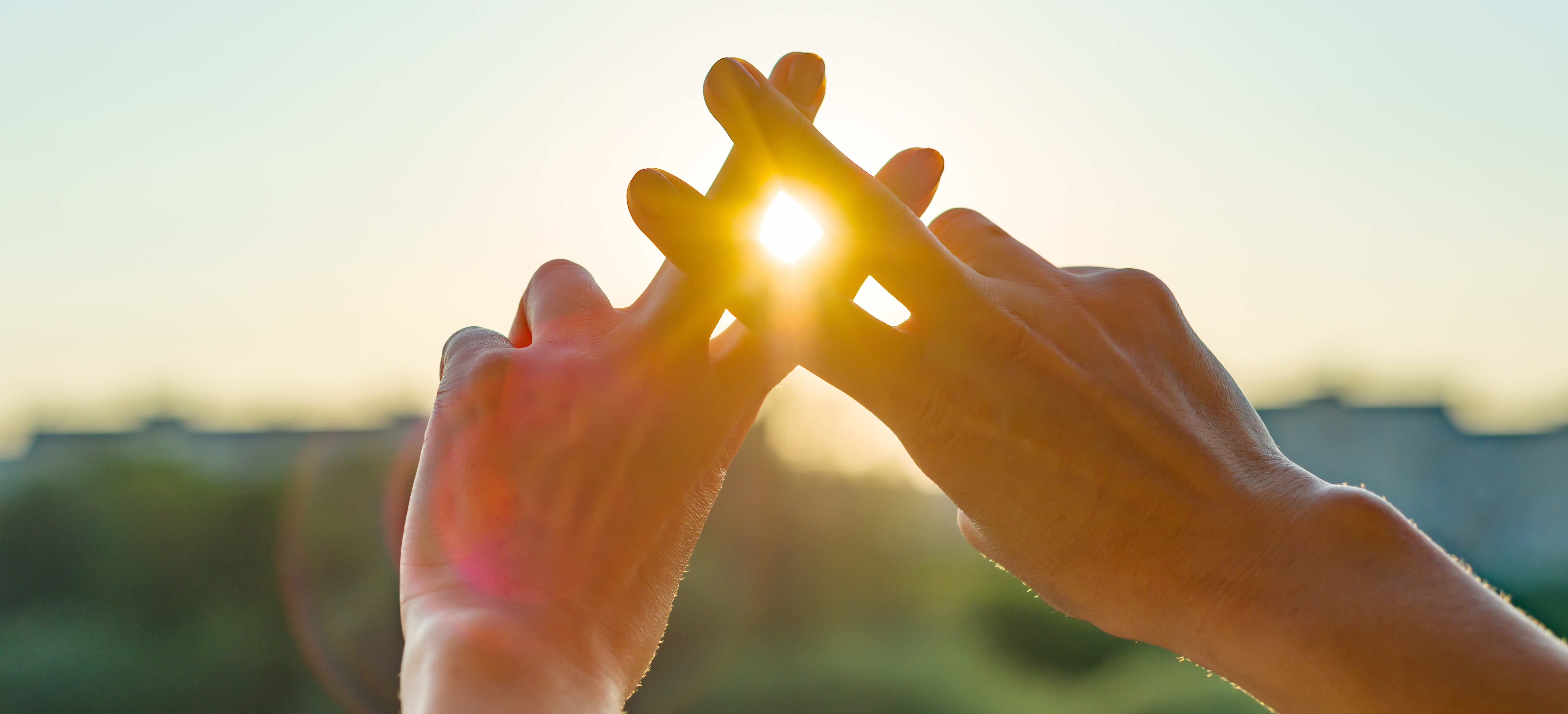 Zwei H&auml;nde formen ein Kreuz, durch das warmes Sonnenlicht scheint &ndash; Symbol f&uuml;r Hoffnung und Glauben.